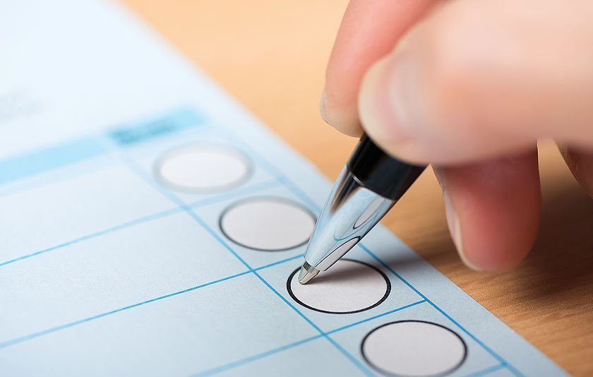 Hand mit Kugelschreiber beim Ankreuzen eines Wahlzettels Hand mit Kugelschreiber beim Ankreuzen eines Wahlzettels