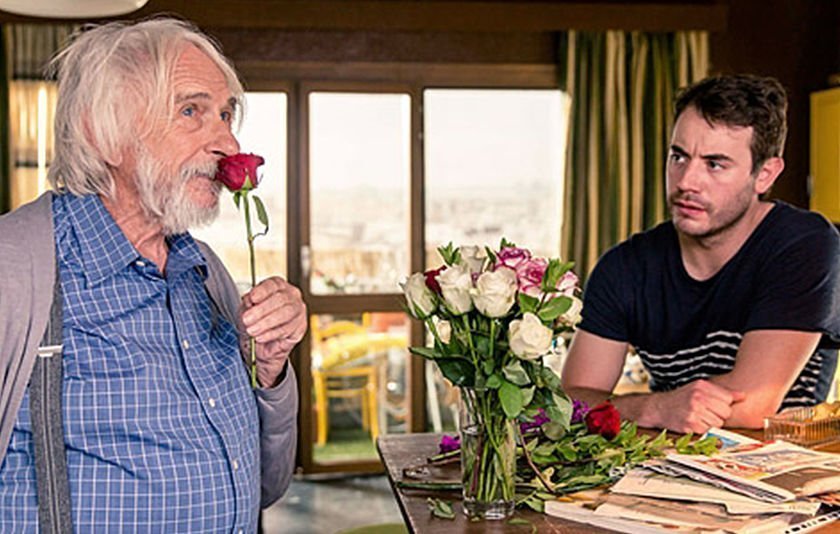 links Senior mit Rose, Blumen in der Mitte, rechts jüngerer Mann