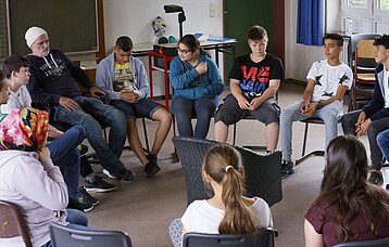 Der Lehrer und seine Schülerinnen und Schüler sitzen im Kreis