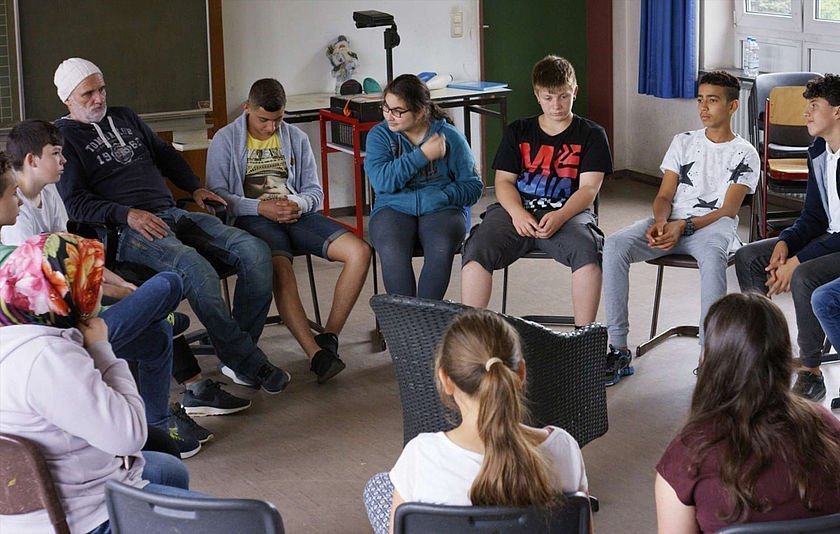 Der Lehrer und seine Schülerinnen und Schüler sitzen im Kreis