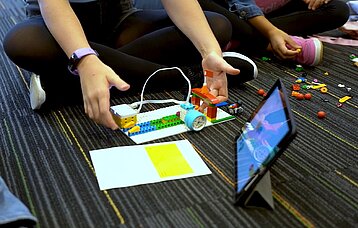 Schülerhände, iPad, Legosteine, Bastelpapier