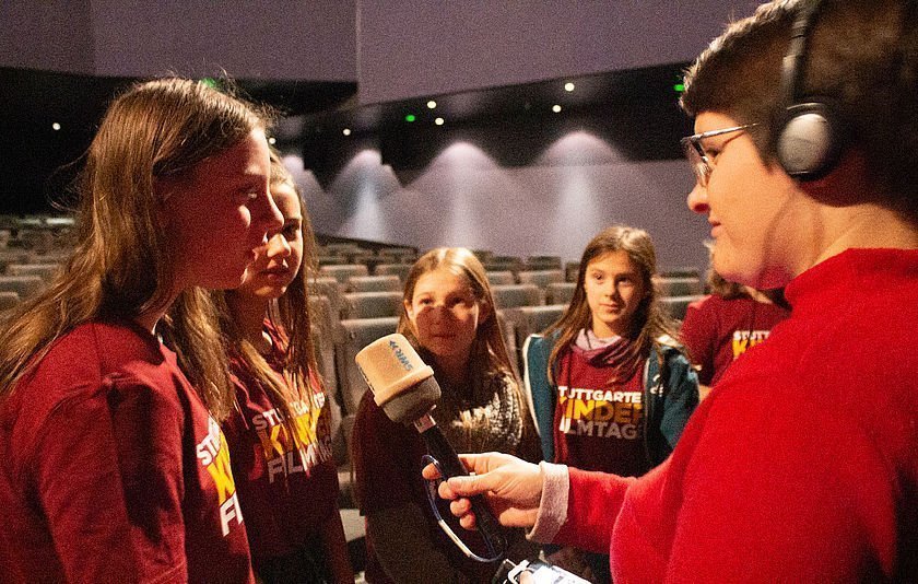 Journalist hält Mikro. Mädchen der Kinderjury antworten im Kino