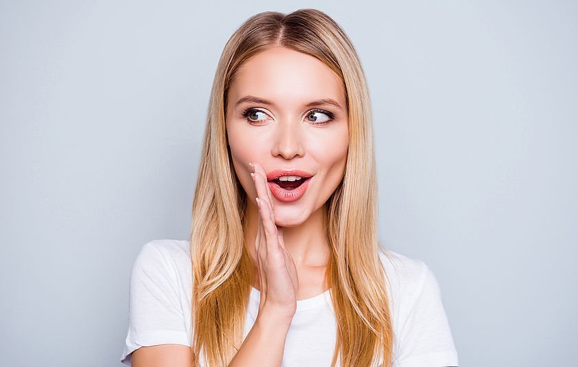 Junge Frau hat die Hand am Mund, um flüstern zu simulieren Junge Frau hat die Hand am Mund, um flüstern zu simulieren