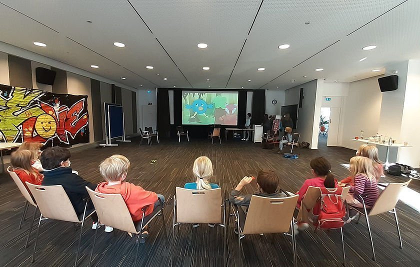 Stuhlreihe mit Kindern von hinten im Filmsaal auf Projektionswand blickend