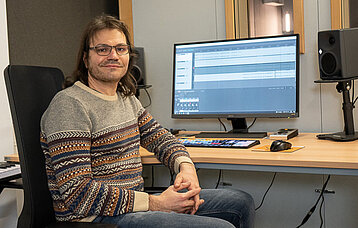 Referent sitzt vor seinem Computer und wendet sich dem Betrachter zu